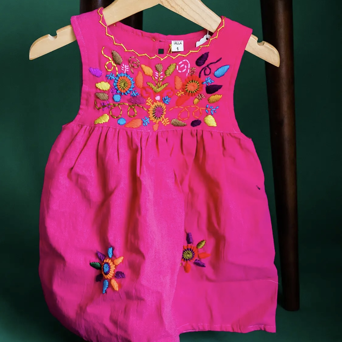 Pink dress with colorful floral embroidery on a hanger against a dark background