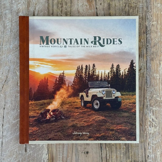Book titled 'Mountain Rides' with a jeep and sunset scene on a wooden surface