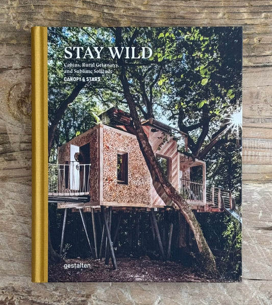 Book titled 'Stay Wild' with a treehouse design on the cover, placed on a wooden surface.
