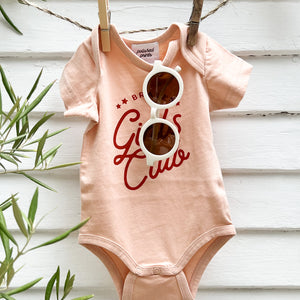 toddler sunglasses in white hanging in a toddlers pink onesie that says "Girls Club"