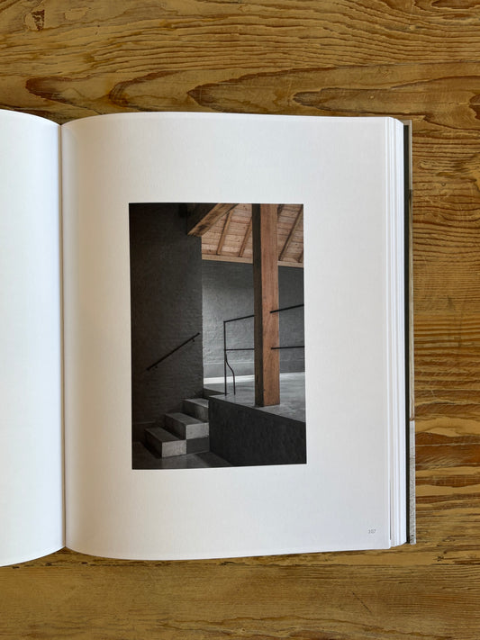 An open book lying on a wooden surface, showing a printed architectural photograph of dark stairs and a wooden column on the right page.