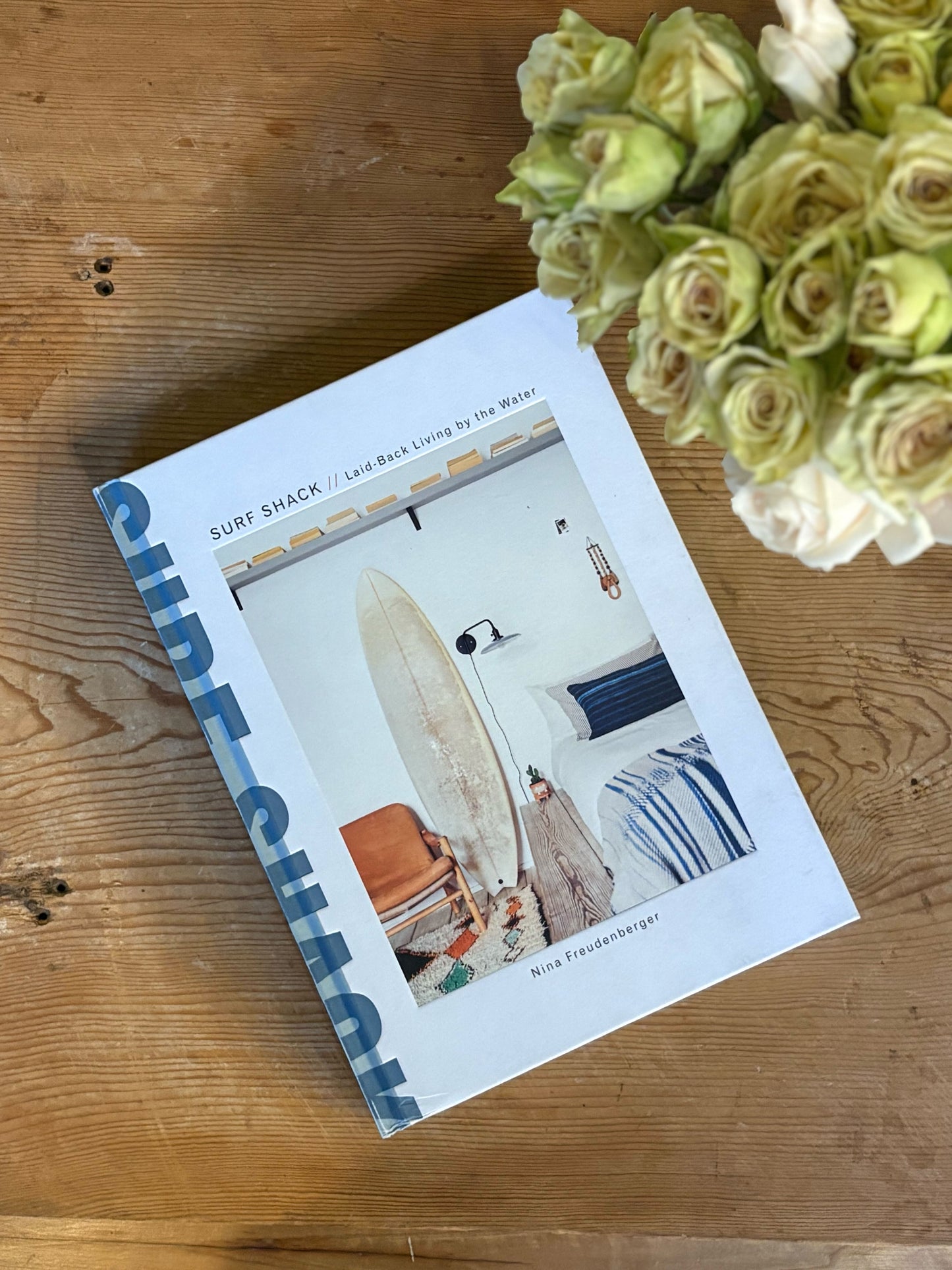 Book titled 'Surf Shack' on a wooden surface with a bouquet of flowers.