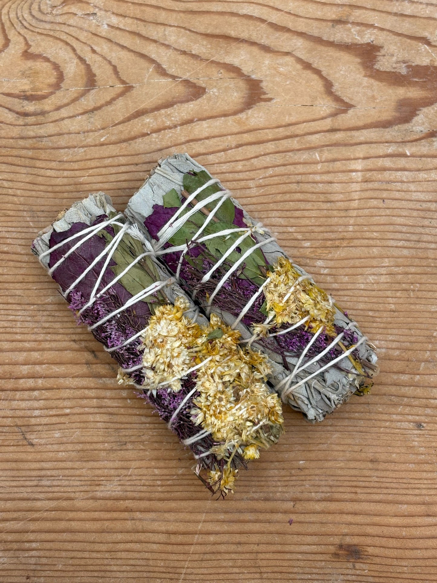 Two sage smudge sticks with gold and purple elements on a wooden surface