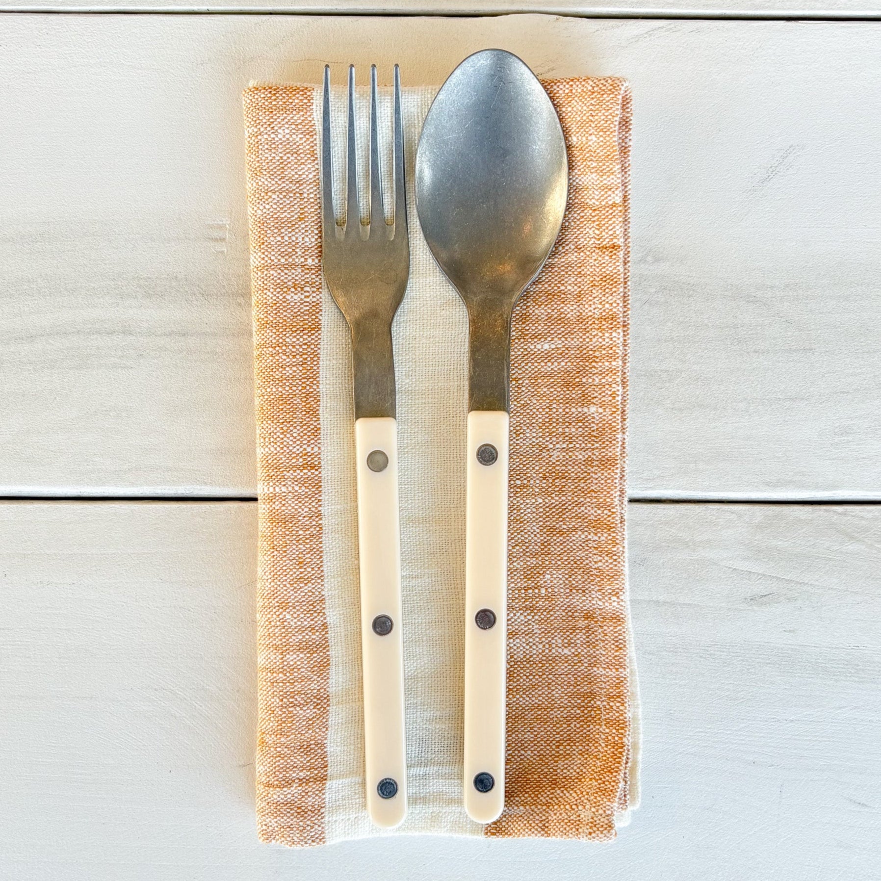 Silver fork and spoon on a wooden napkin with a light wood background