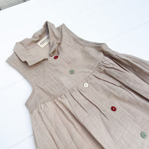 sleeveless tan linen kid's dress with colored buttons down front and a collar