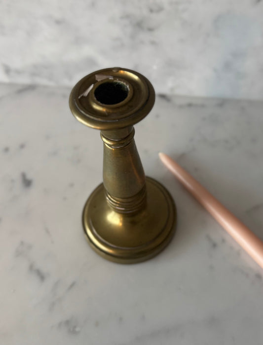 Brass candlestick holder on a marble surface with a pink candle