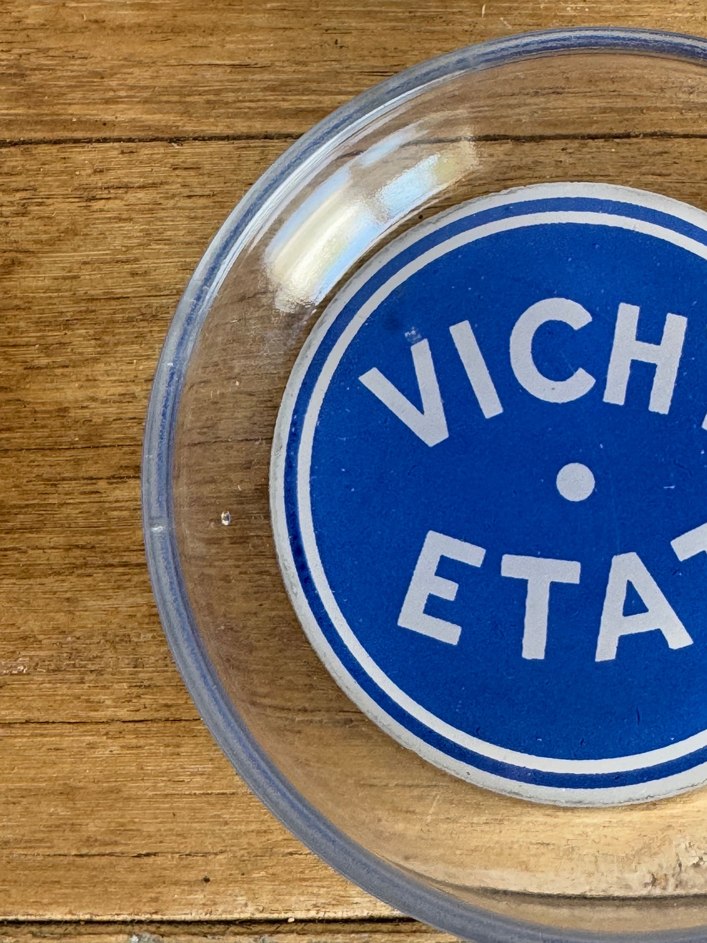 Close-up of a Vichy Etat logo on a clear container lid against a wooden background