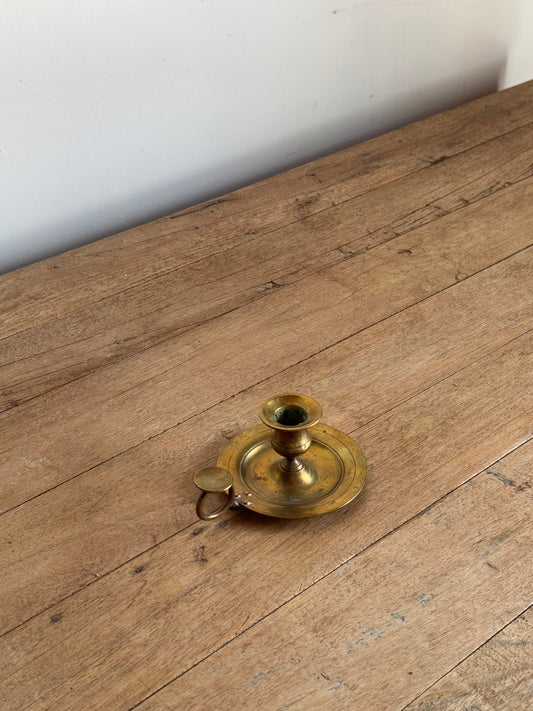Brass candlestick on a wooden surface with a white wall background