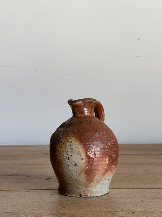 Small brown ceramic vase against a light gray wall and wooden surface