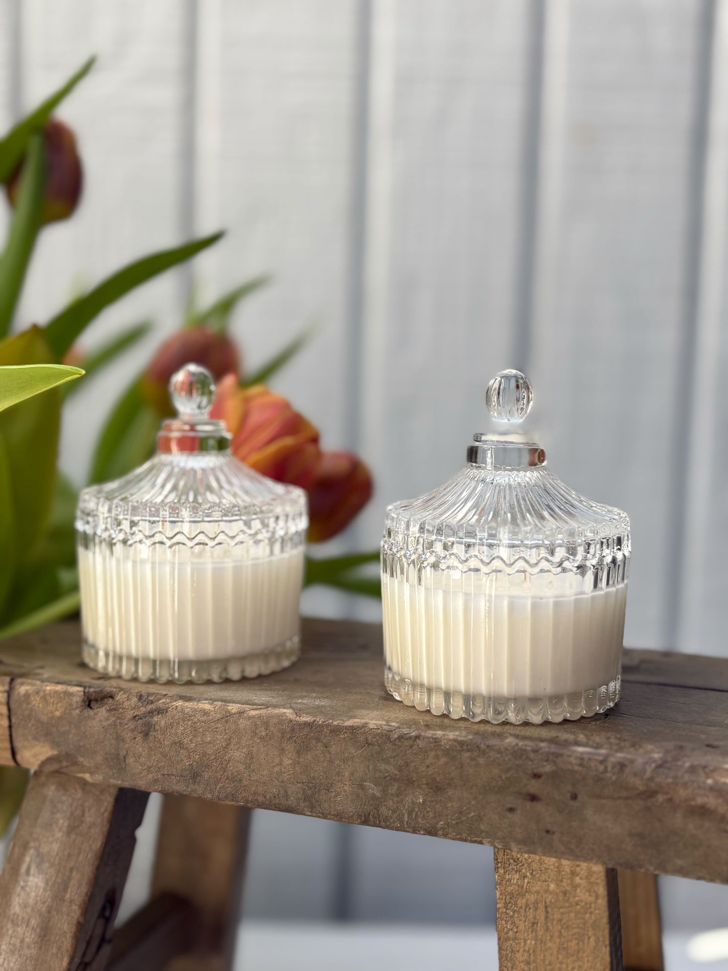 Two glass jars with decorative lids on a wooden surface with a blurred floral background.
