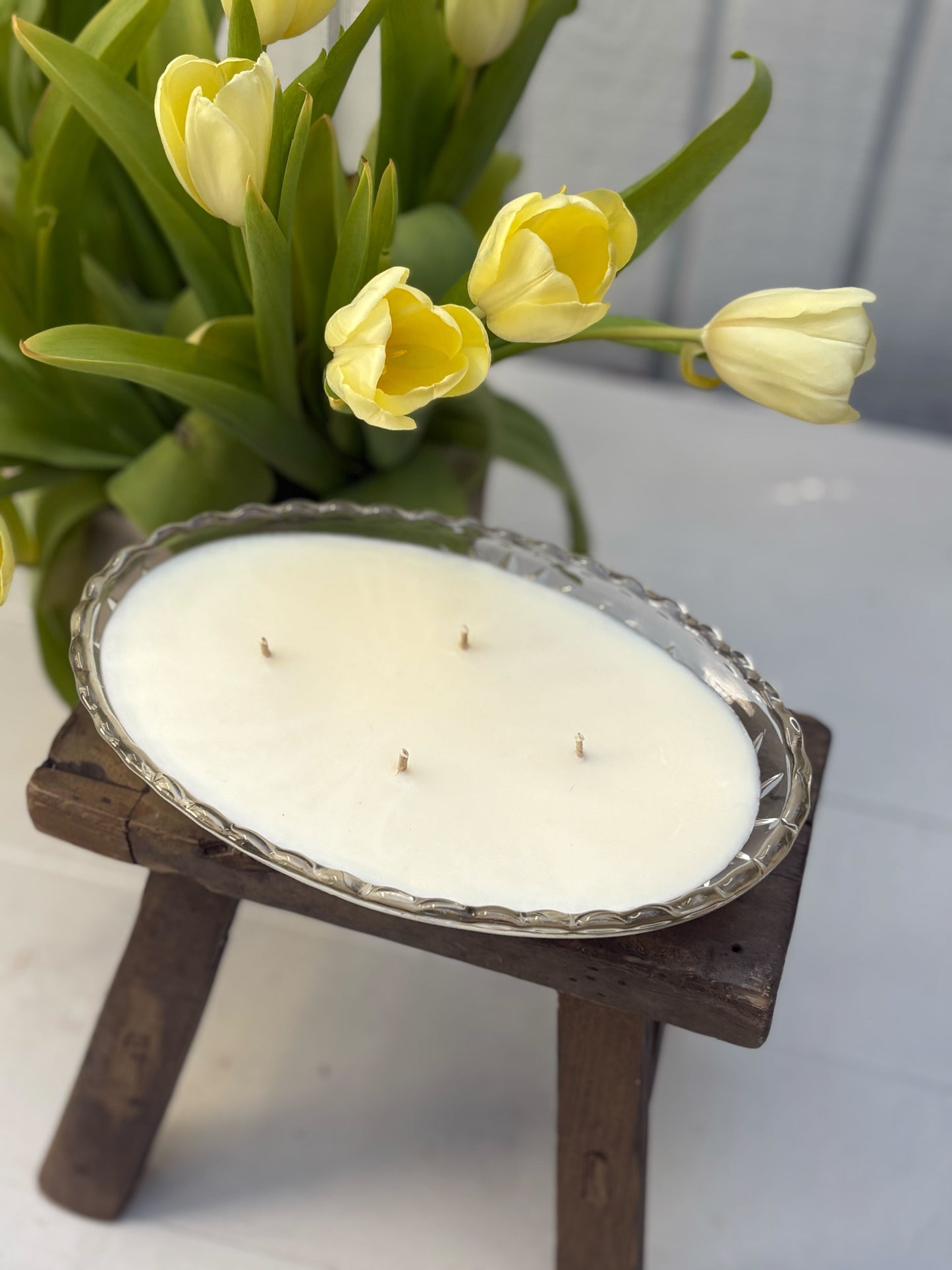 Candle on a small wooden stand with yellow tulips in the background