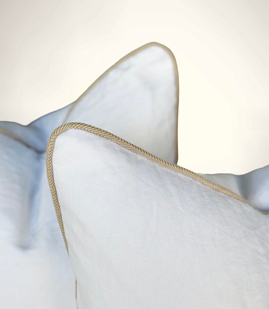 Close-up of a white pillow with beige piping on a light gray background