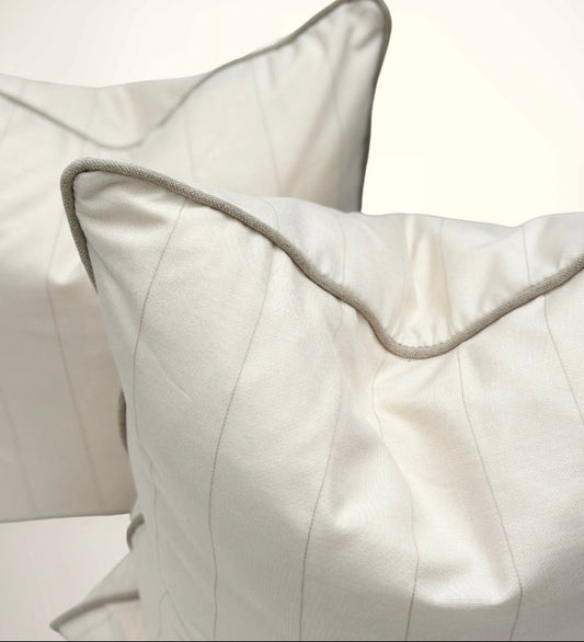 Close-up of two white pillows with gray piping on a light background