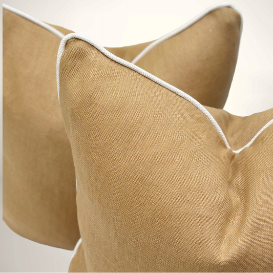 Close-up of beige pillows with white piping on a light background