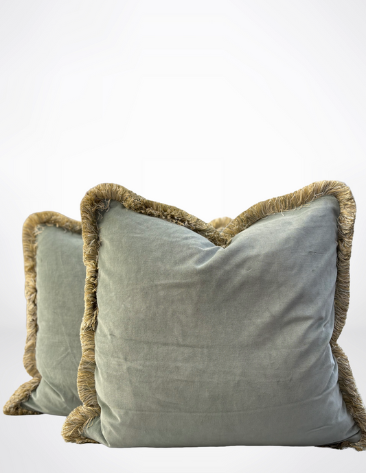 Two sage green pillows with brown fringes on a white background