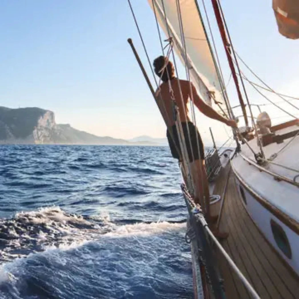 Man on a sailboat in the open sea with mountains in the background