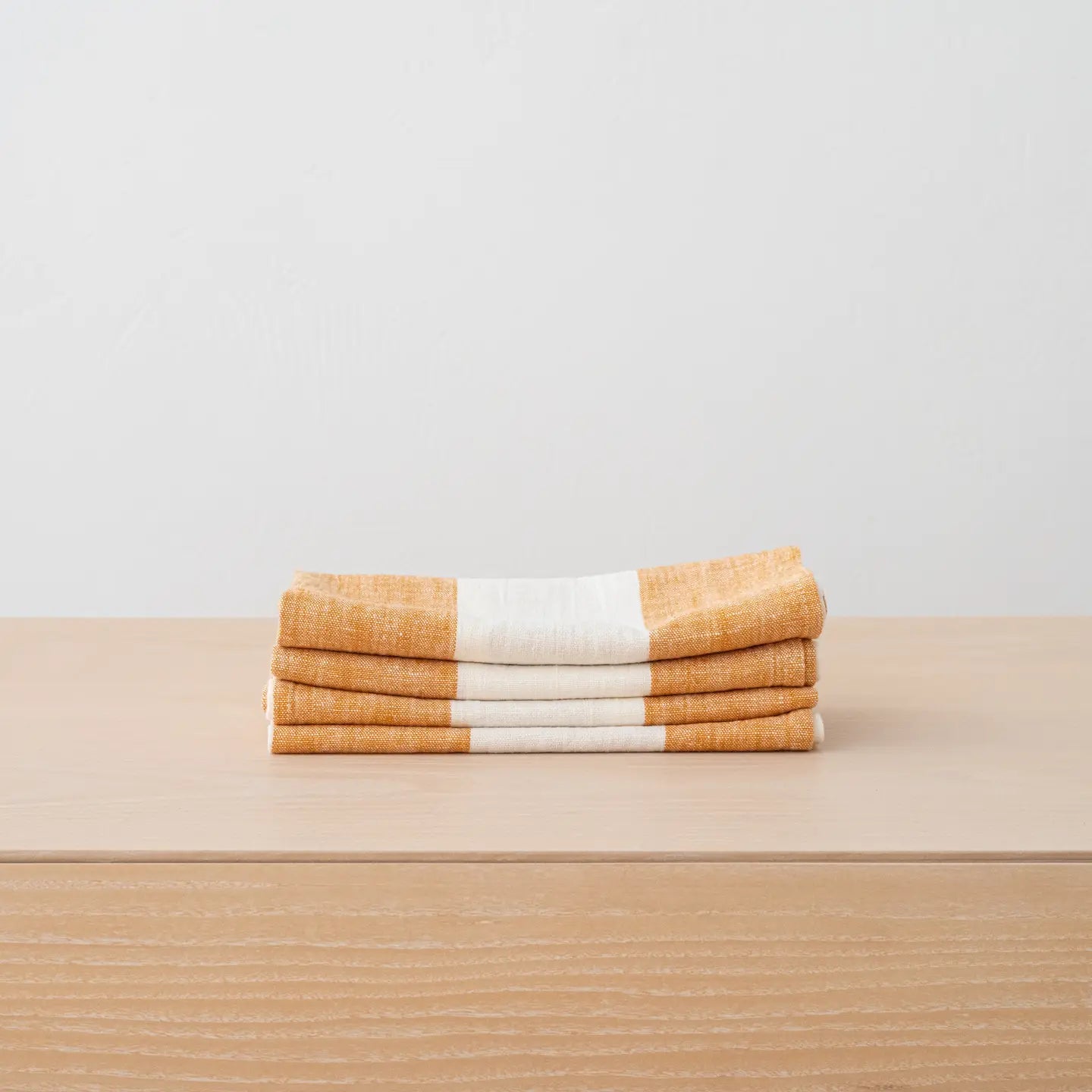 Stack of folded towels with orange and white stripes on a beige surface.