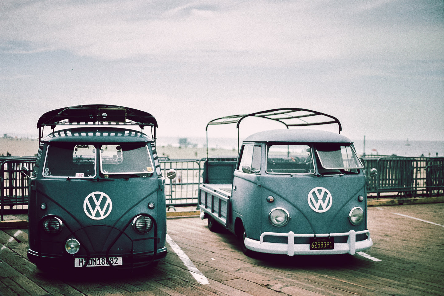 photo of two green vintage VW vans in parking lot at the beach