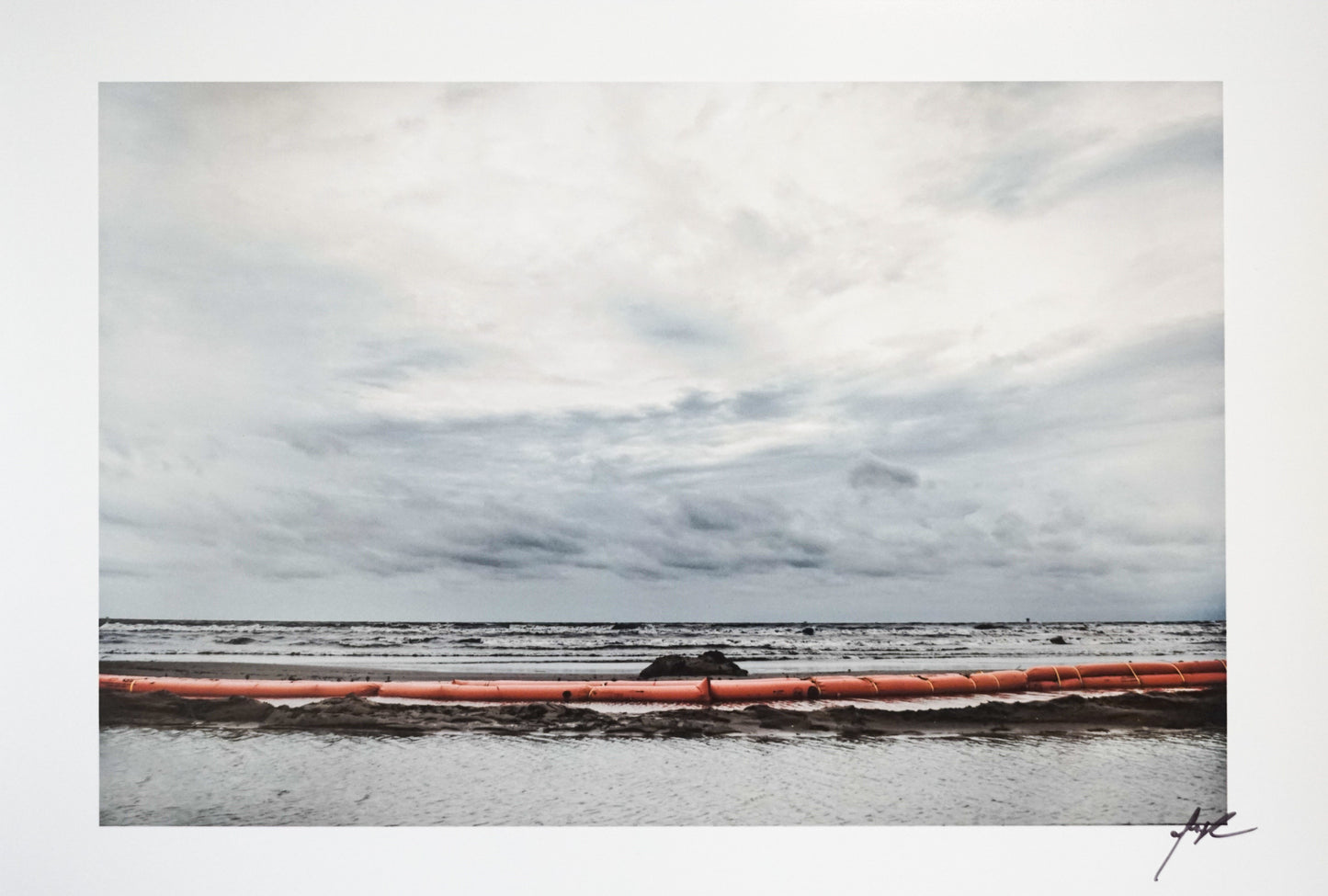 ocean with gray clouds and red barrier at shore line Edit alt text