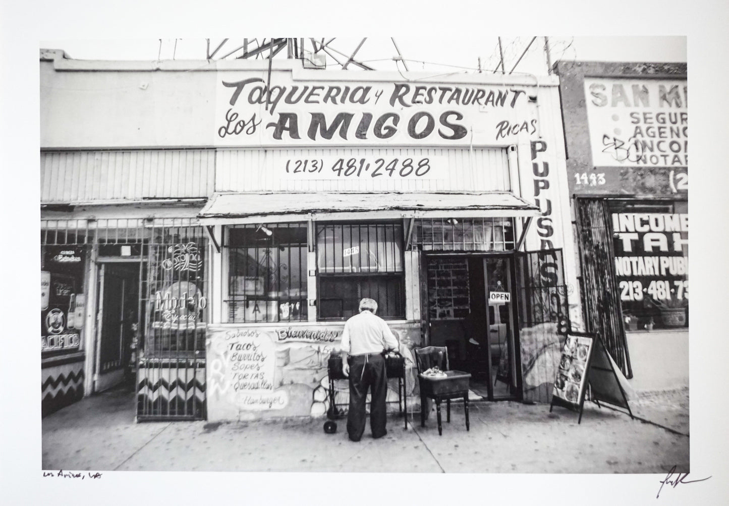 black and white photo of front of an old taqueria with man standing in front Edit alt text