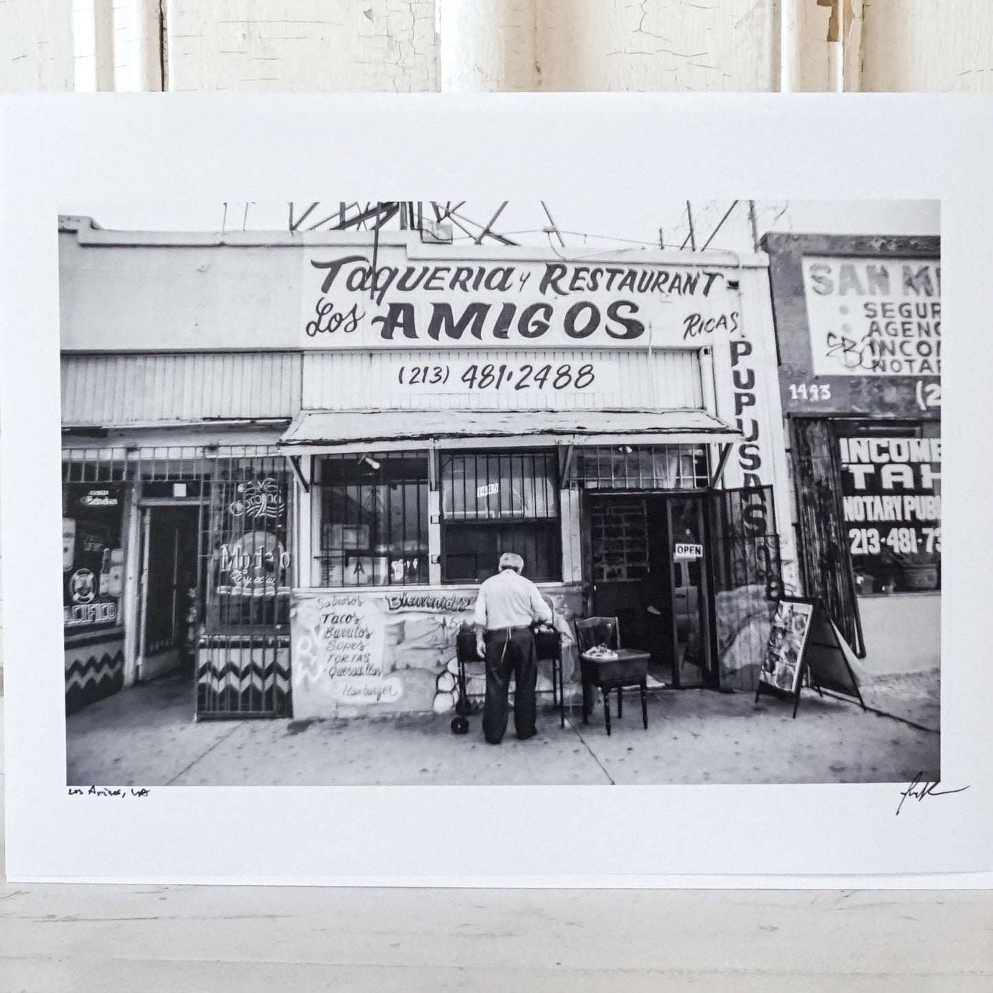 black and white photo of front of an old taqueria with man standing in front Edit alt text
