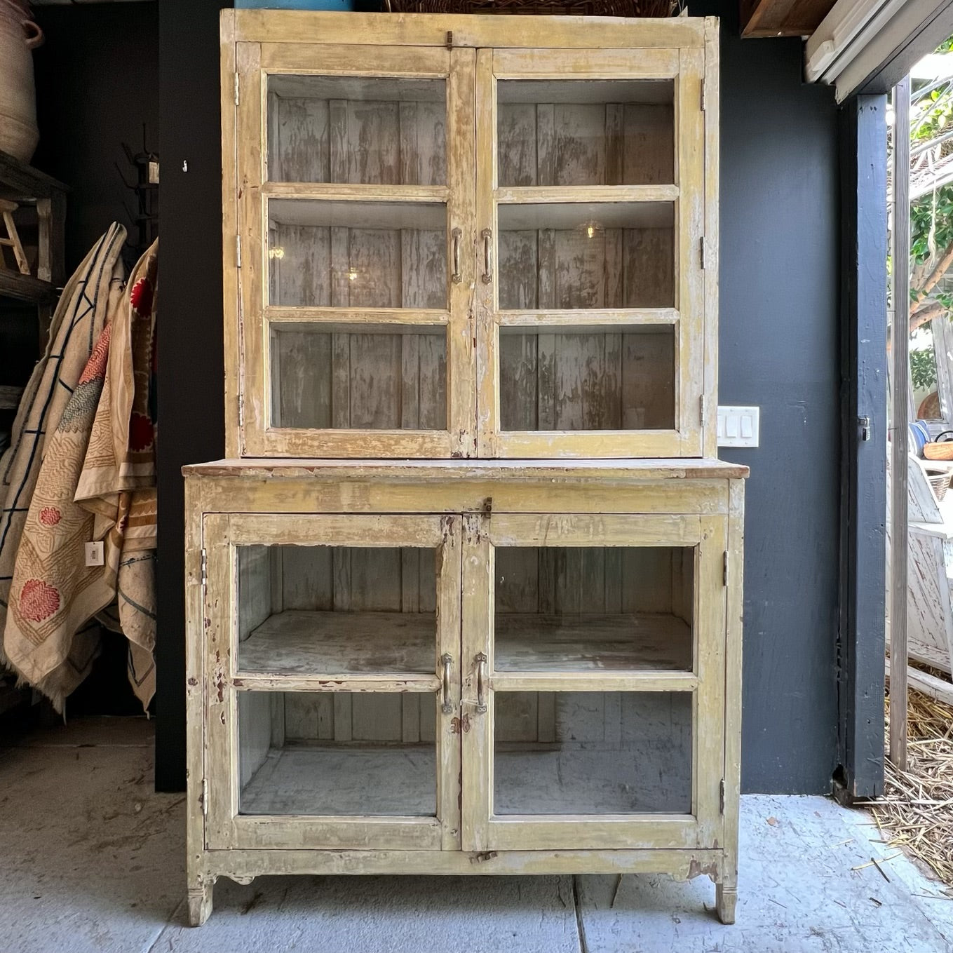 rustic hutch of old wood with distressed butter yellow paint finish, glass doors on top and bottom