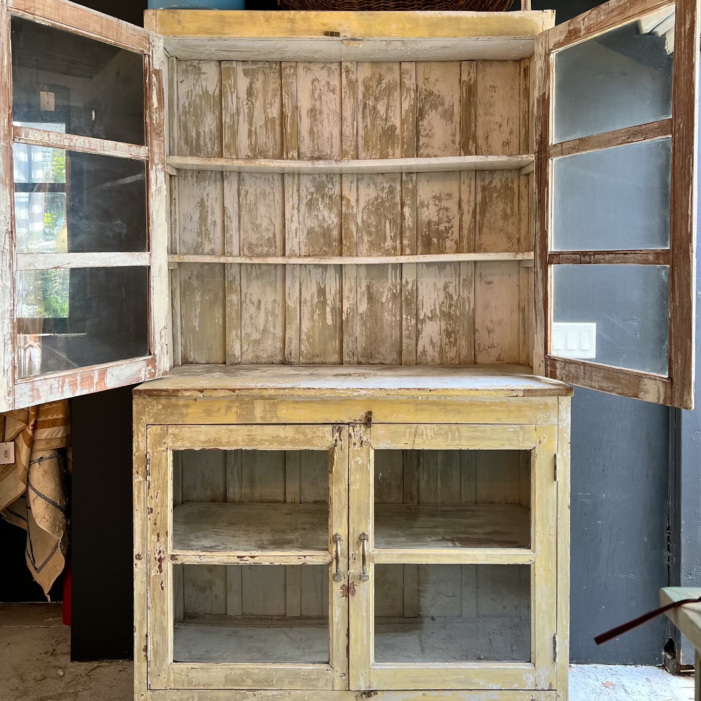 rustic hutch of old wood with distressed butter yellow paint finish, glass doors on top and bottom