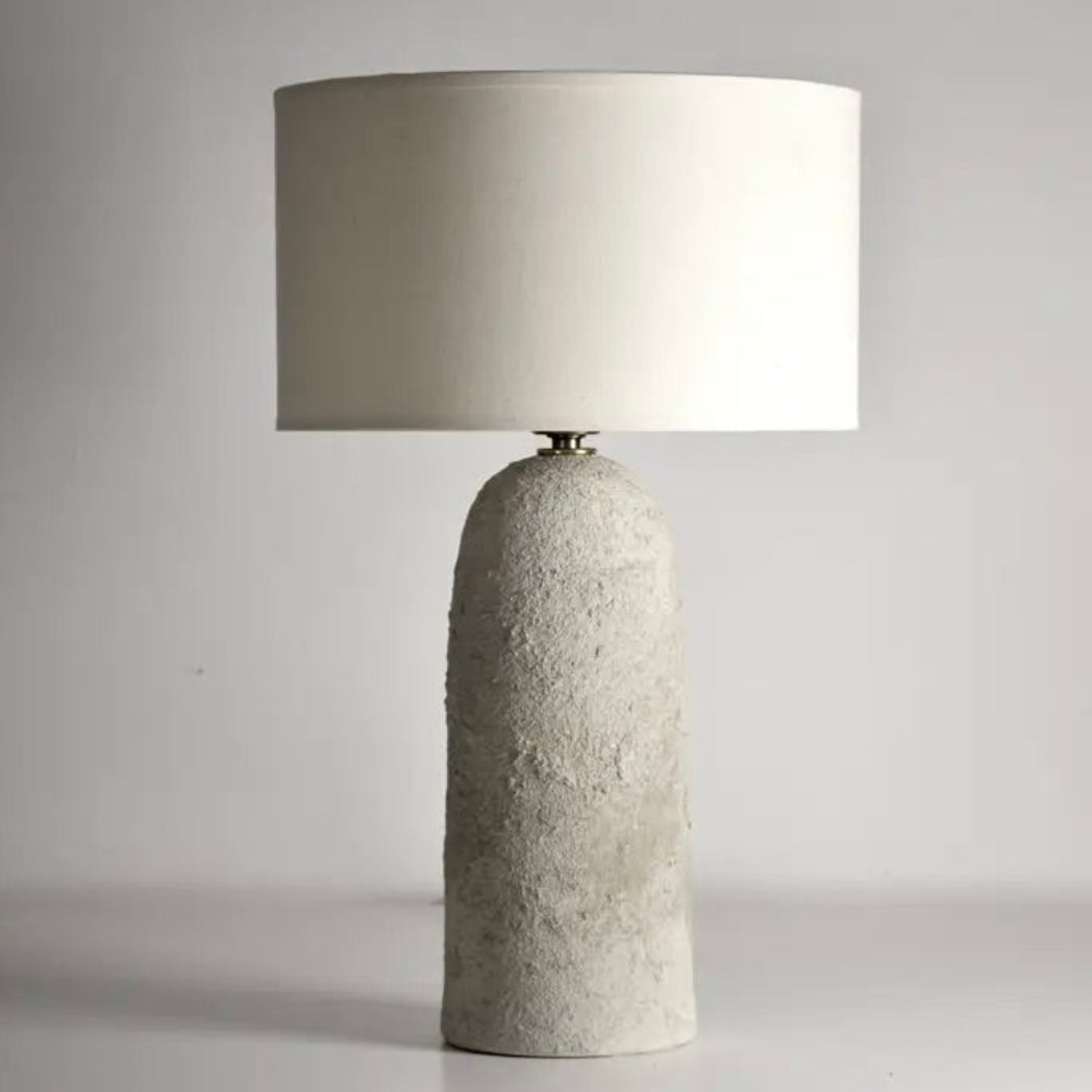 Table lamp with textured concrete base and white shade on a gray background