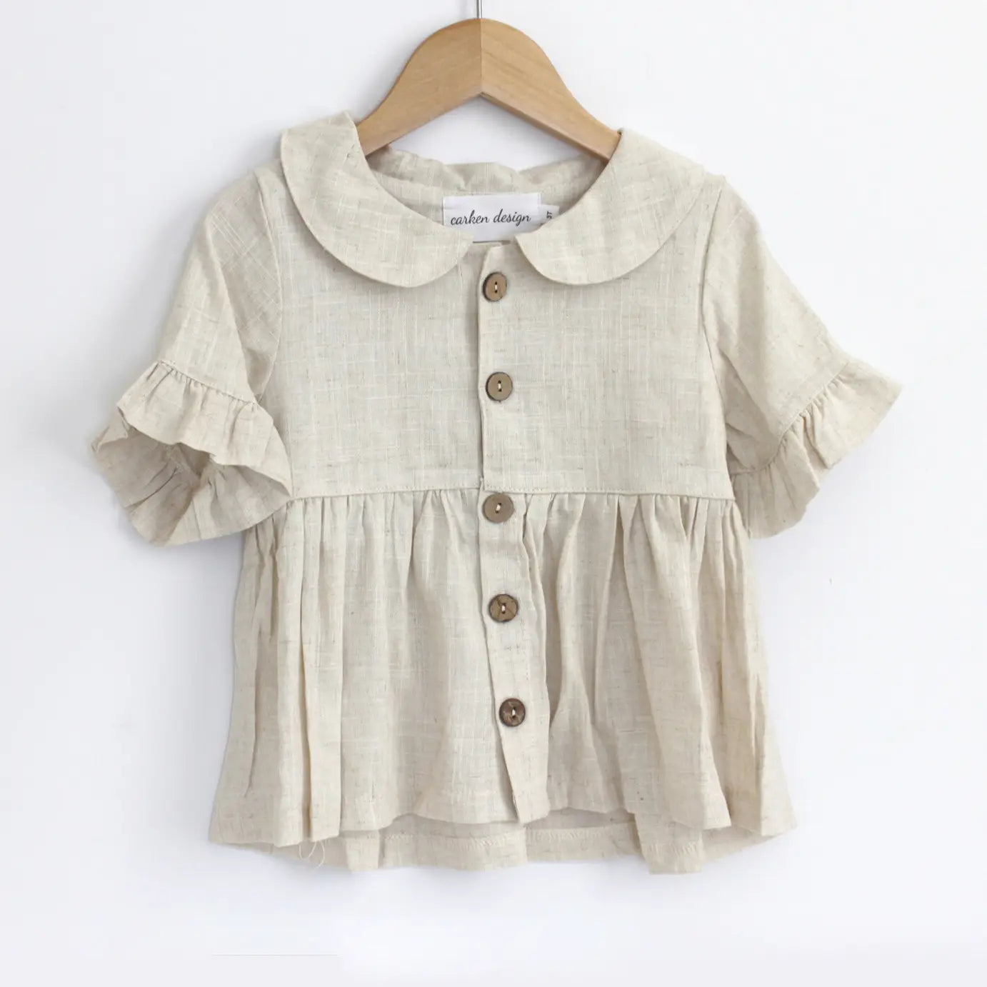 Beige blouse with ruffled sleeves and collar on a wooden hanger against a white background