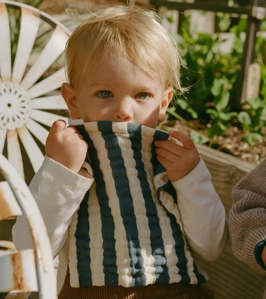 Child holding a striped towel in front of their face with a garden background