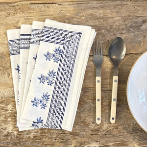 Set of white napkins with blue floral patterns on a wooden surface with cutlery.