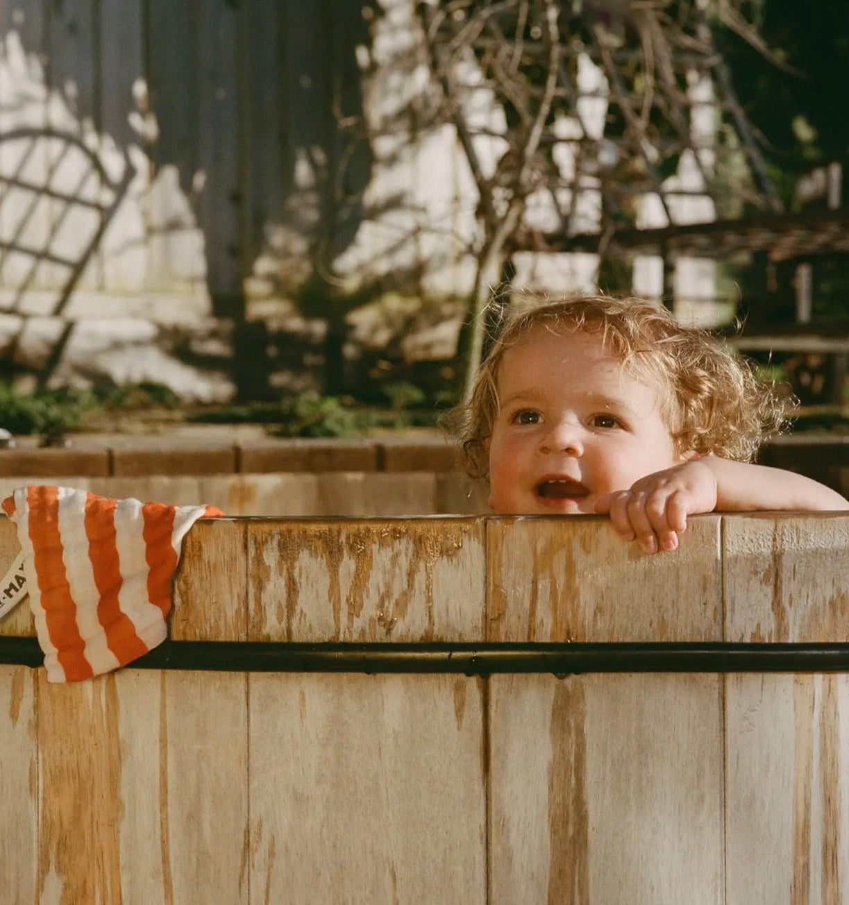 Child peeking over a wooden fence with a striped towel in the background