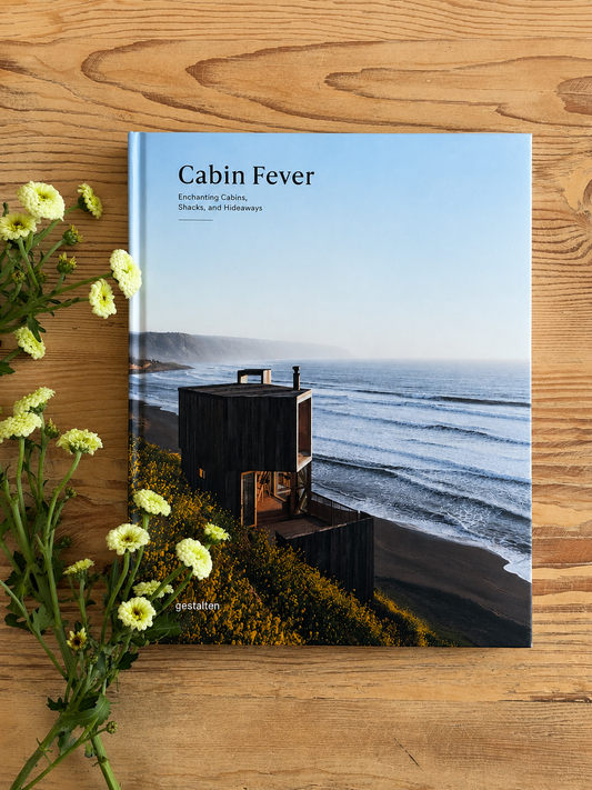 Book titled 'Cabin Fever' on a wooden surface with flowers.