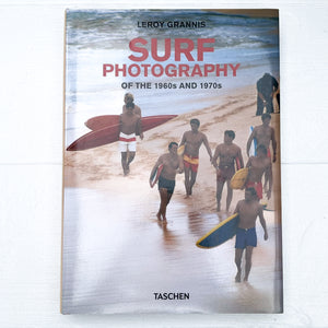 cover of surfing book "Surf Photography of the 1960's and 1970's" with a vintage photo  of several men at beach carrying surf boards