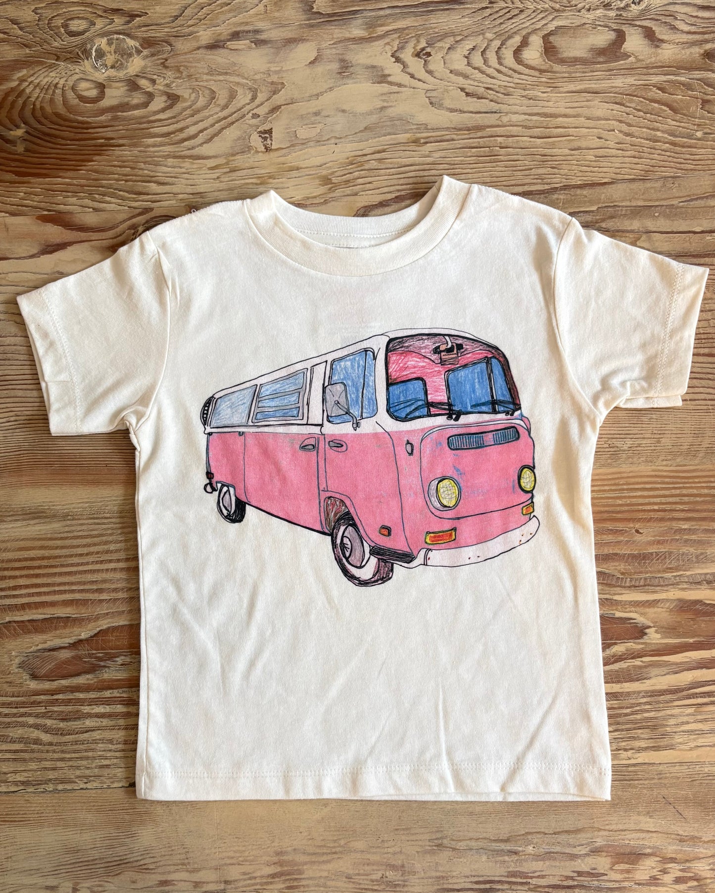 White t-shirt with a pink van graphic on a wooden surface