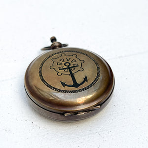 round brass pocket compass with anchor and ship's wheel on front