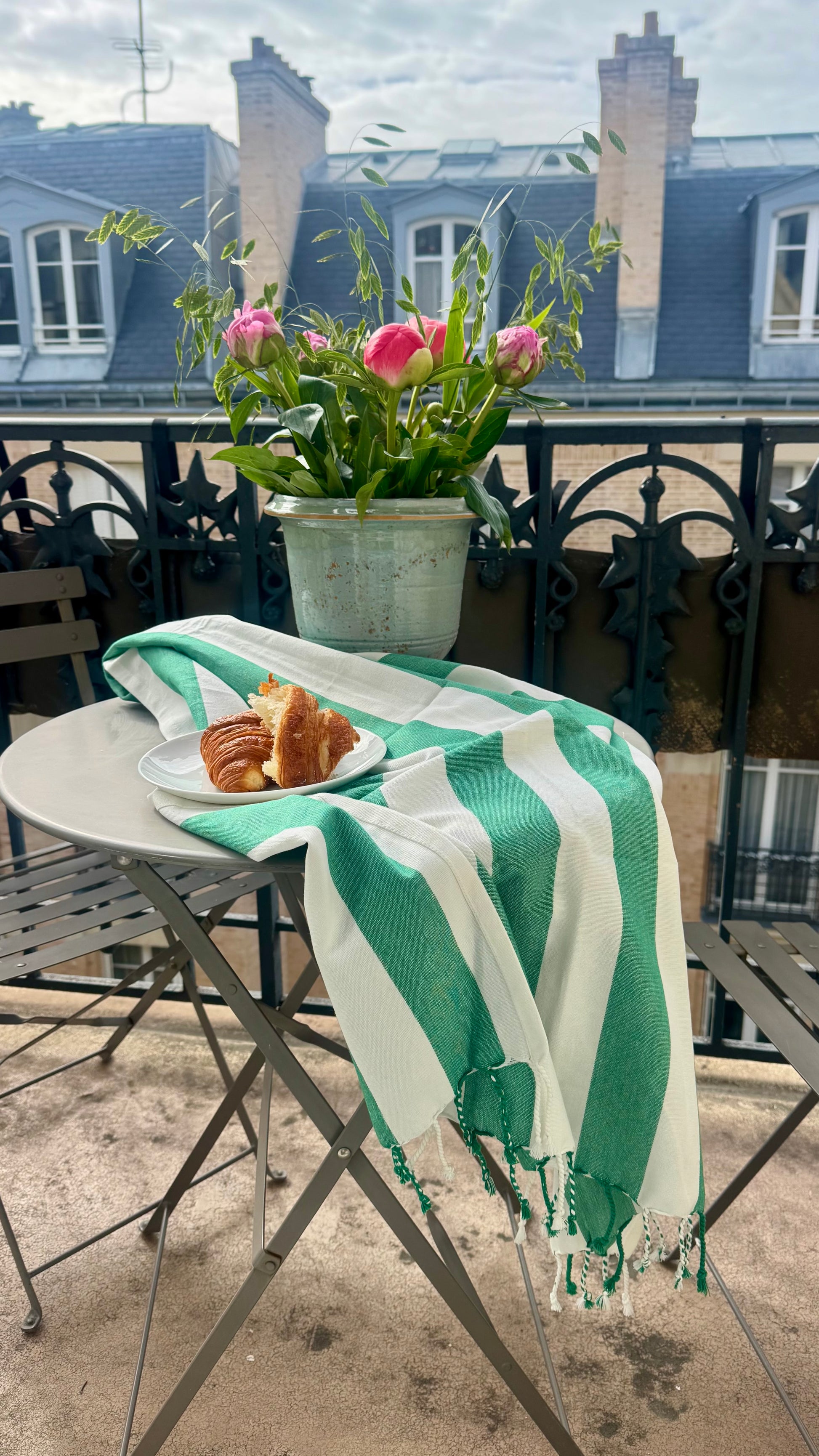 Green and white striped towel draped over a table with a plate of food on a balcony.