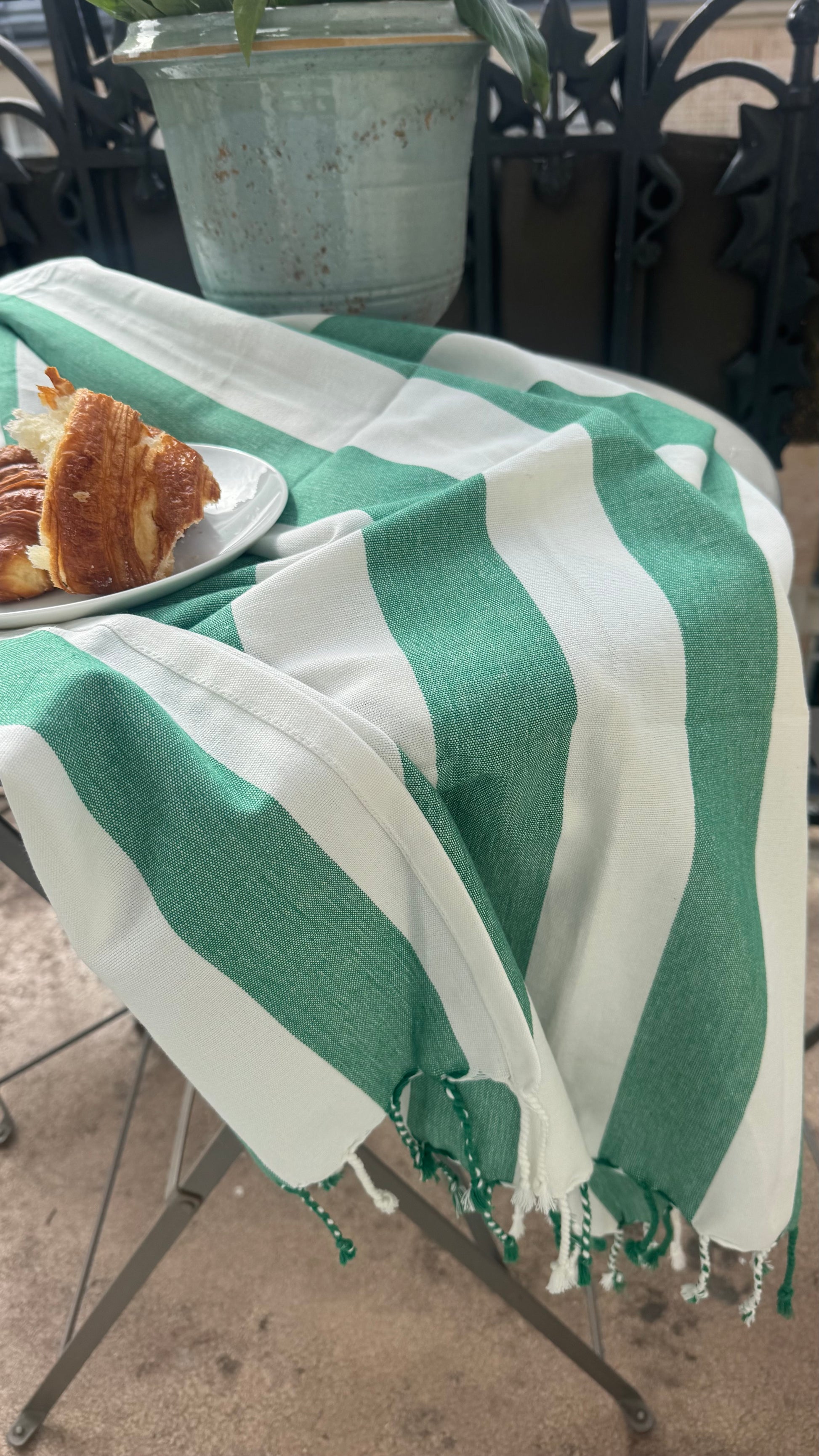 Green and white striped towel on a table with a plate of food in the background.