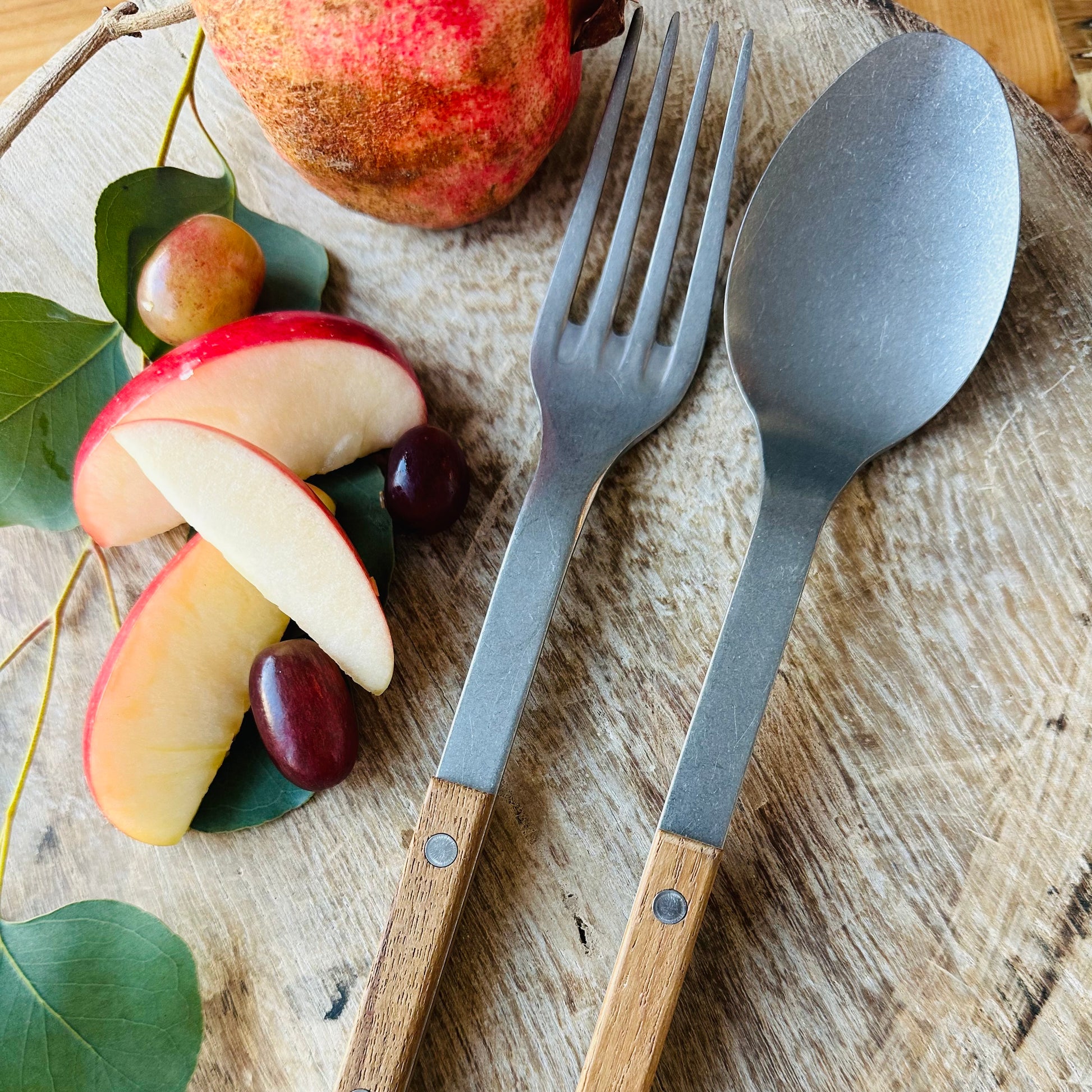 A set of French cutlery flatware on a wooden board, including knives, spoons, and forks with teak handles.