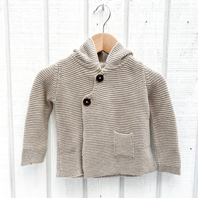 oatmeal colored baby sweater with hood and two black buttons and one small pocket