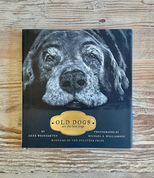 The book 'Old Dogs: Are the Best Dogs' by Gene Weingarten and Michael S. Williamson, featuring a black and white portrait of an older dog on the cover, placed on a light wood grain surface.