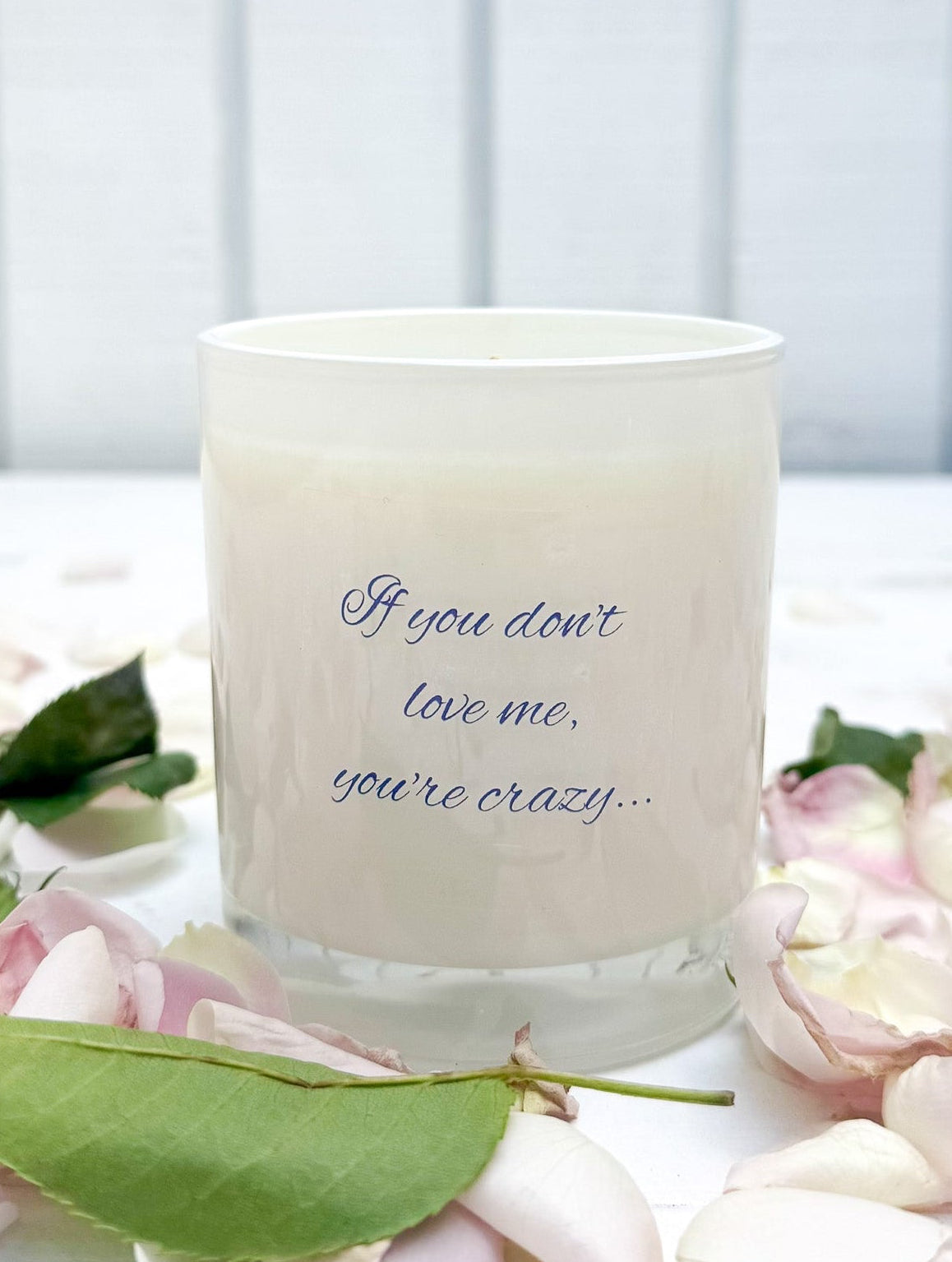 Candle with text on a white surface surrounded by flowers