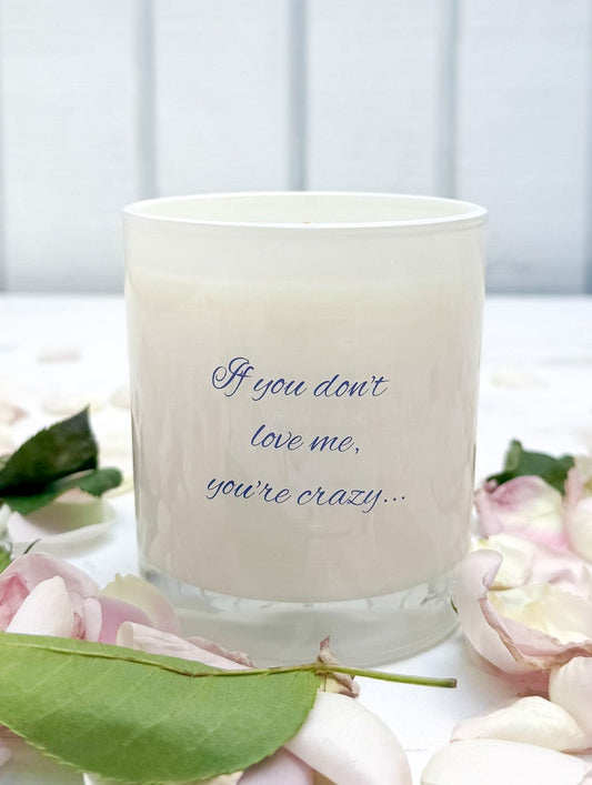 Candle with text on a white surface surrounded by flowers