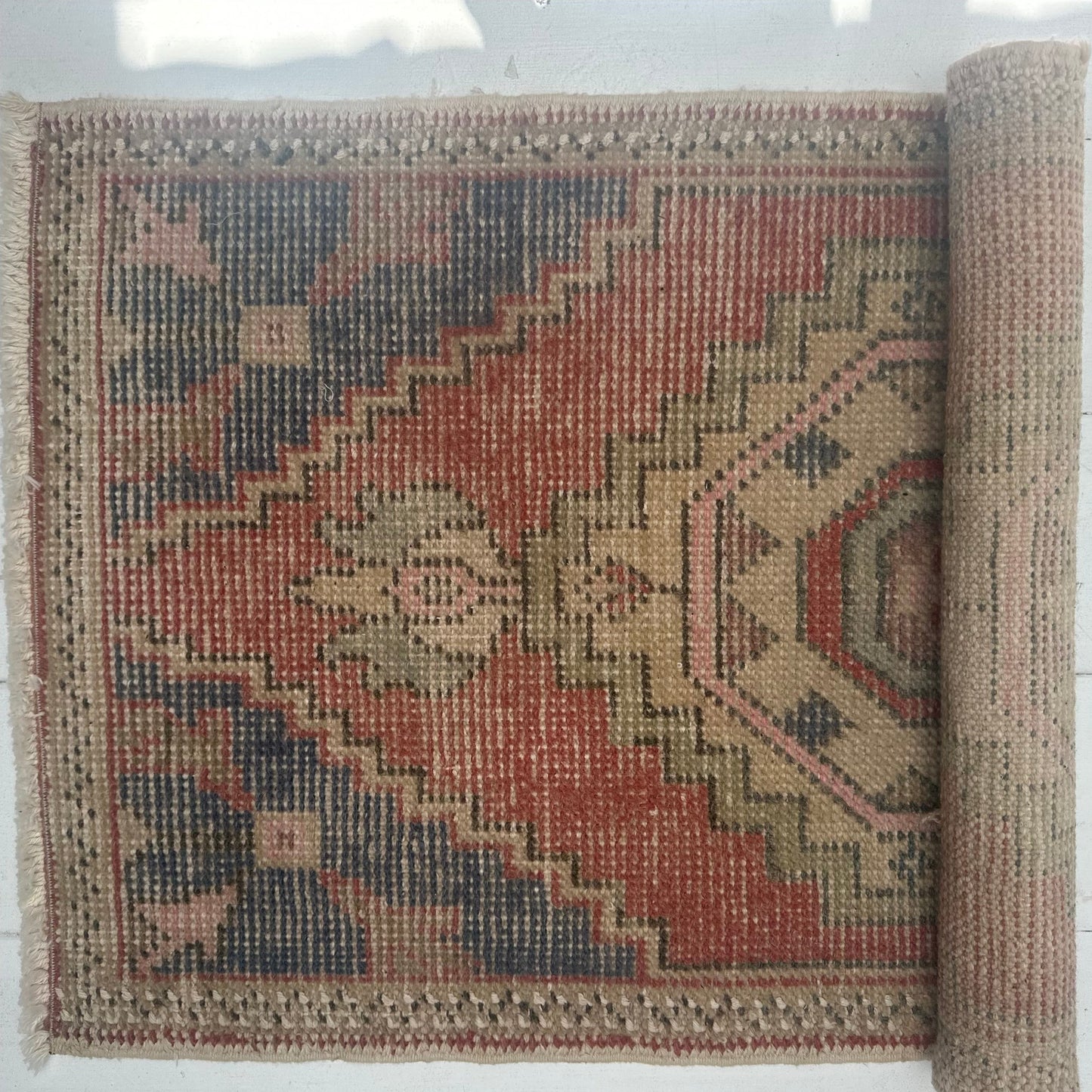 A vintage Turkish rug with geometric patterns, predominantly red and blue, and a beige border.