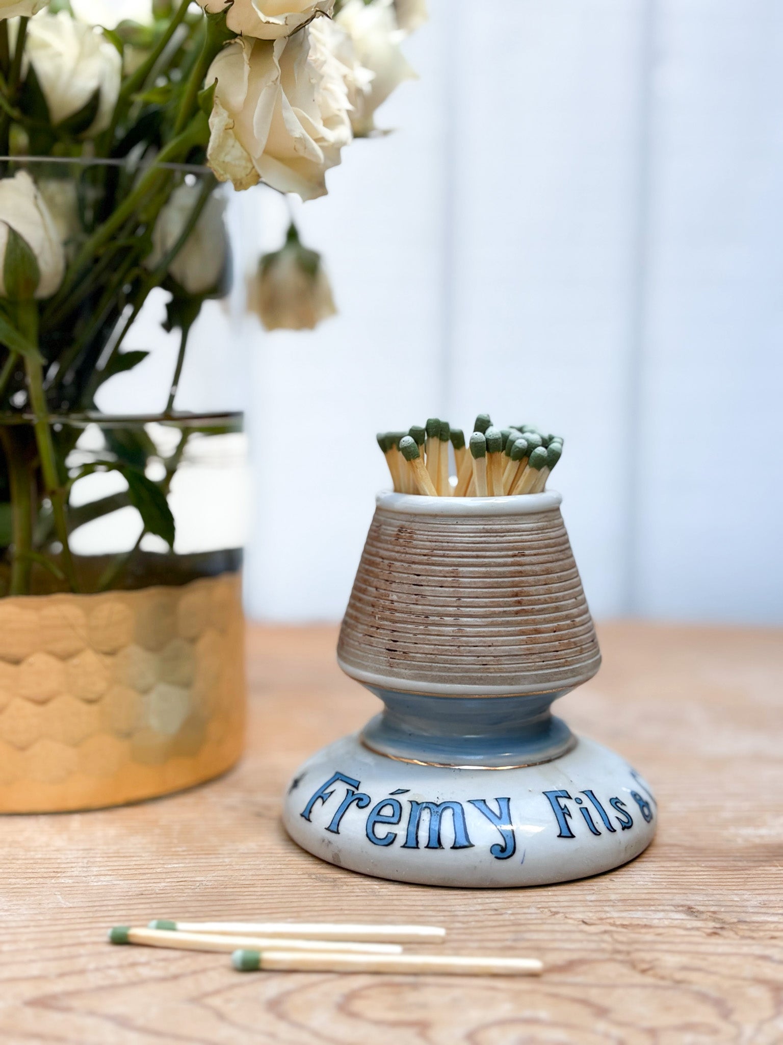 Ceramic match holder with matches on a wooden surface, next to a vase of flowers.