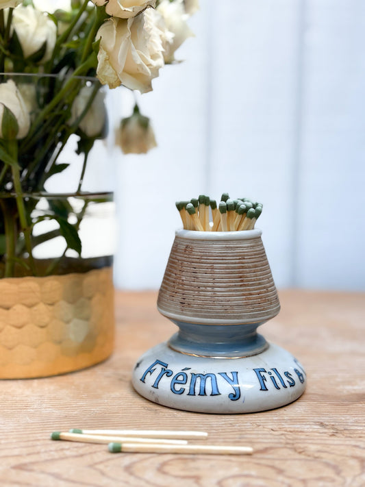 Ceramic match holder with matches on a wooden surface, next to a vase of flowers.