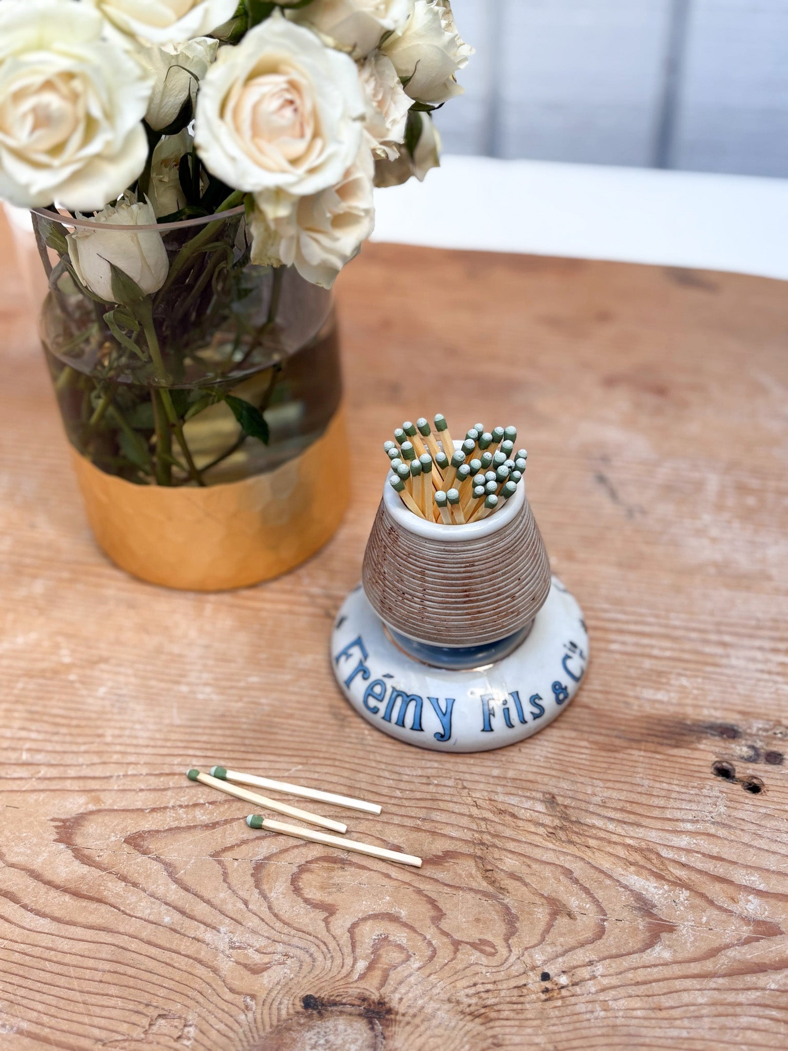 Small ceramic match holder with matches on a wooden table next to a vase of white flowers.
