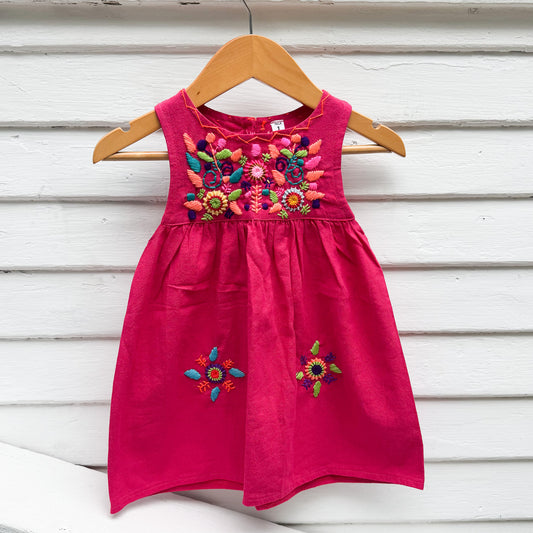 Pink dress with colorful floral embroidery on a wooden hanger against a white background
