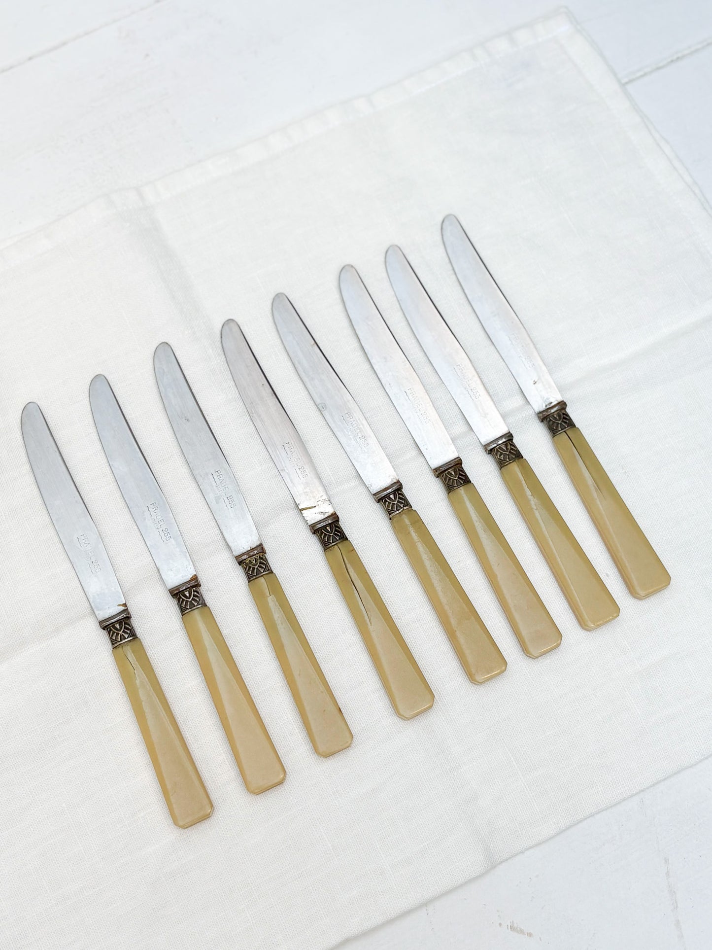 Set of eight knives with beige handles on a white surface