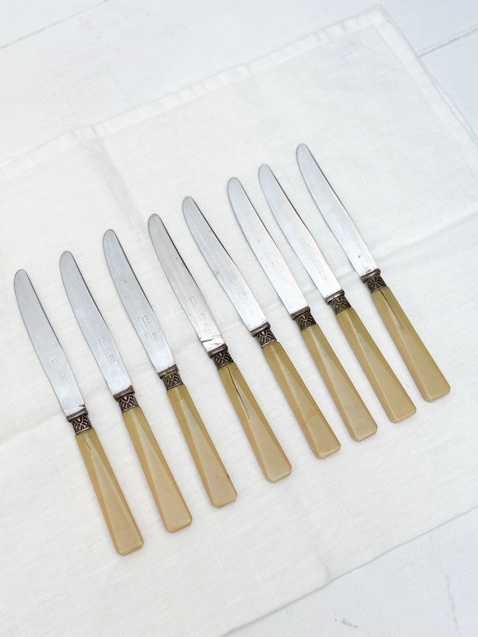 Set of eight knives with beige handles on a white surface